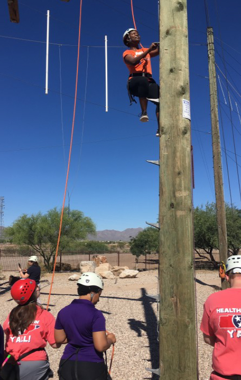 Person climbing pole with 3 people on the ground