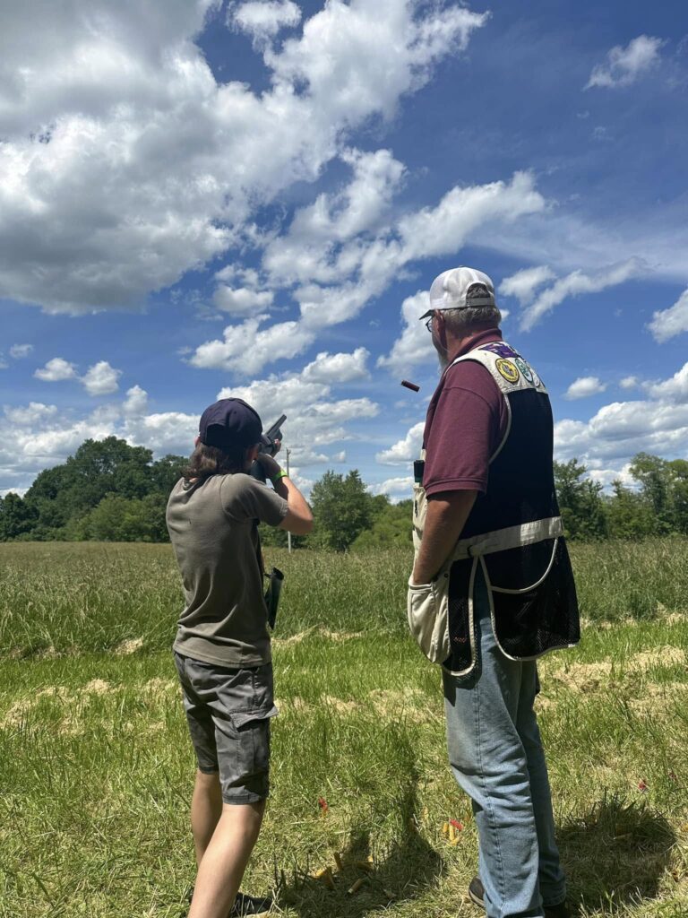 male 4-H'er shooting at a clay target with instructor standing beside him.