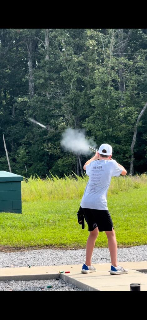 male 4-H'er shooting at a clay target with smoke coming from the barrel.
