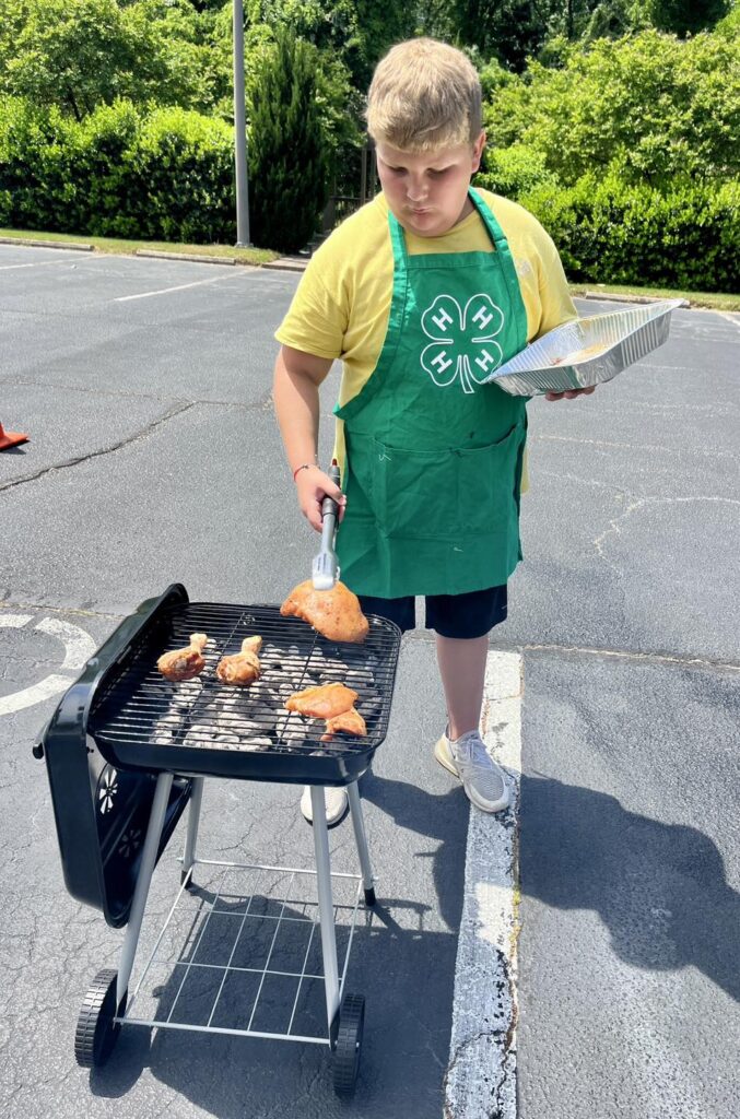 male 4-H youth adding chicken to a grill with tongs.