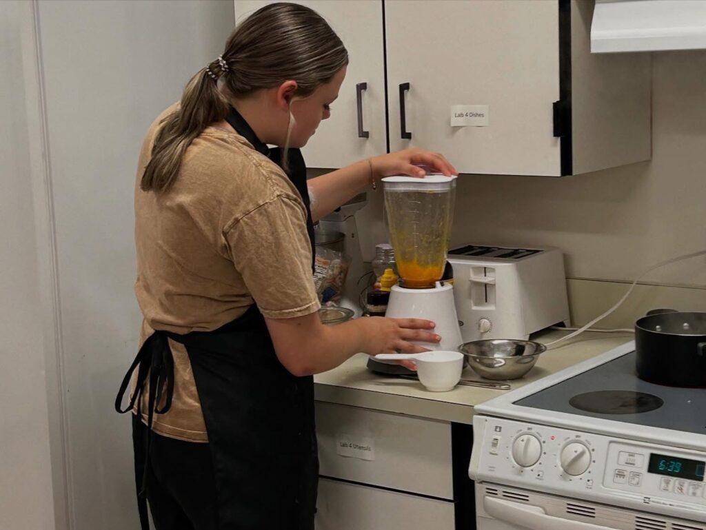 up-close of a female youth in a black apron using a blender in a kitchen.