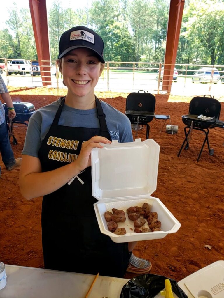 female 4-H'er showing off cooked meats in a to-go container ready for judging.