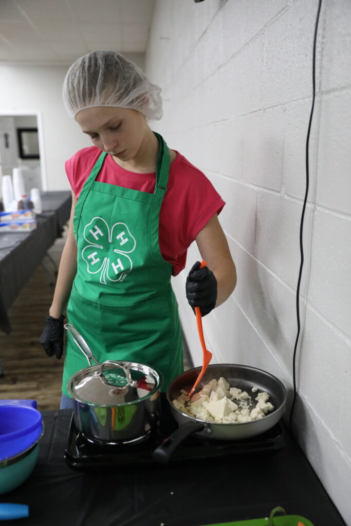female youth mixing tofu in a skillet.