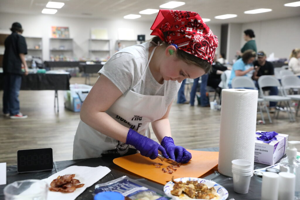 female youth chopping up strips of bacon into pieces.